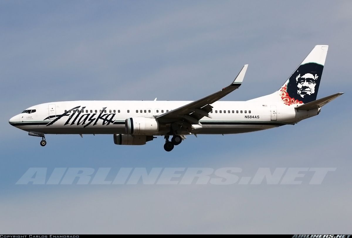 an alaska airlines jet flying in the sky with its landing gear down and it's nose painted