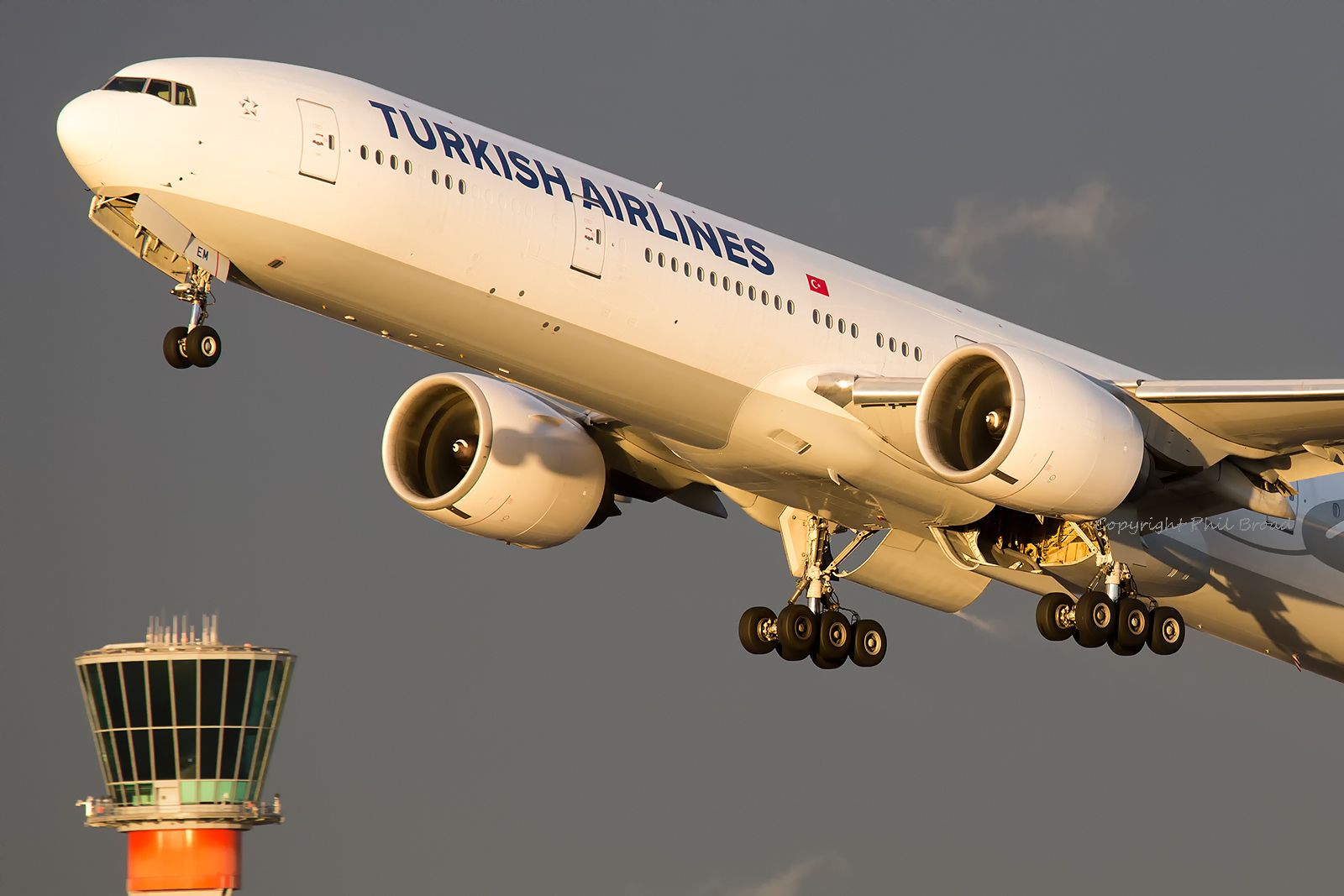a large jetliner flying through a cloudy sky next to an airport control tower with the word turkish airlines on it's side