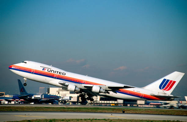 United Airlines Boeing 747-100 taking-off from Runway 25R with an American Airlines 767 parked at the terminal behind.