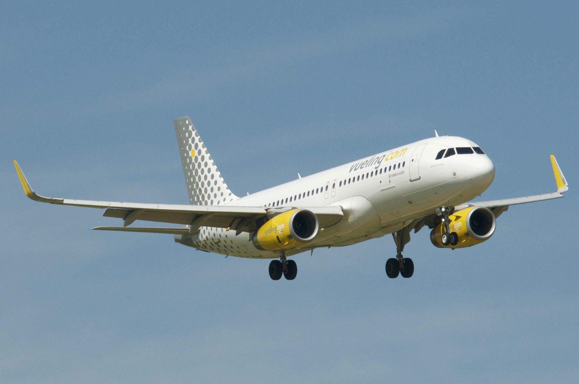 a white and yellow jet airliner flying in the sky with it's landing gear down