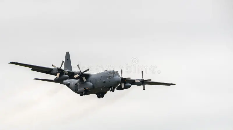 Lockheed Martin C-130 Hercules in flight with a cloudy sky backdrop. The aircraft, a four-engine turboprop military transport plane, features a gray exterior, high wings, and distinctive propellers. Its robust, utilitarian design is evident, optimized for cargo and personnel transport. Landing gear is visible, suggesting approach for landing or takeoff. The image captures a moment in aerial maneuver, highlighting the aircraft's capability and design suited for versatile missions. C130 stock imag
