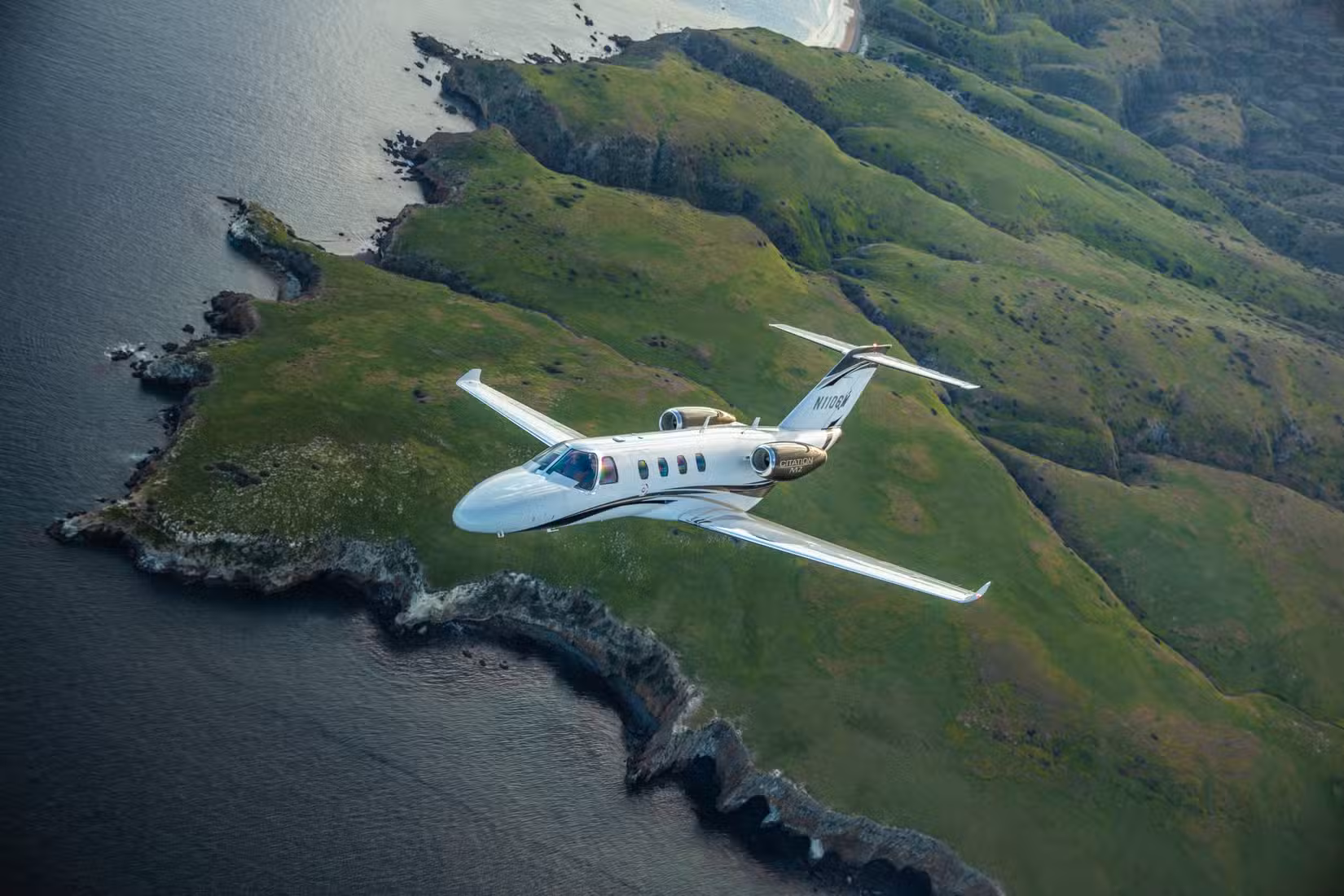A Cessna Citation M2 flying near a coastline.