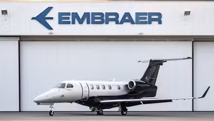 An Embraer Phenom 300E parked right outside of an aircraft hangar.