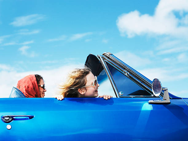 girl (8-10) leaning head over side of convertible car, woman driving - convertible car side view stock pictures, royalty-free photos & images