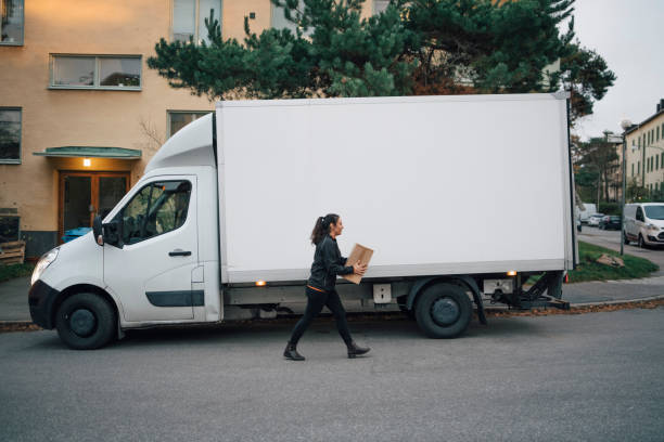 female worker carrying box while walking by delivery van on street in city - delivery truck side view stock pictures, royalty-free photos & images