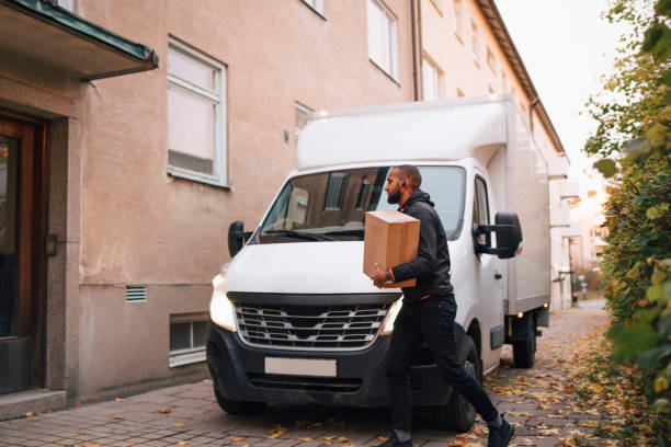 side view of man carrying box while walking by delivery van in city - delivery truck side view stock pictures, royalty-free photos & images