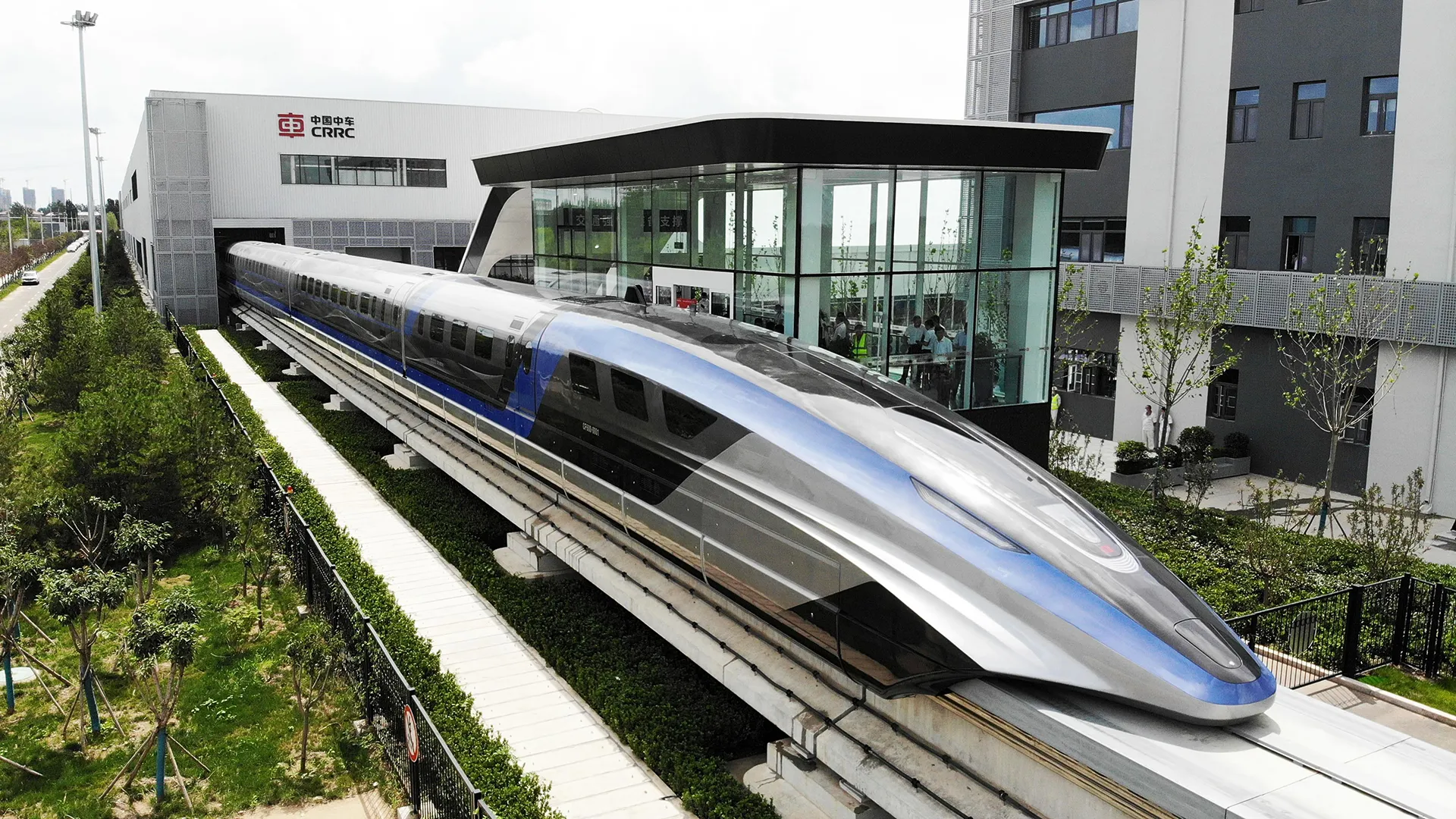 China's new silver and blue maglev train on elevated tracks outside a modern glass and concrete building in Qingdao, Shandong Province.