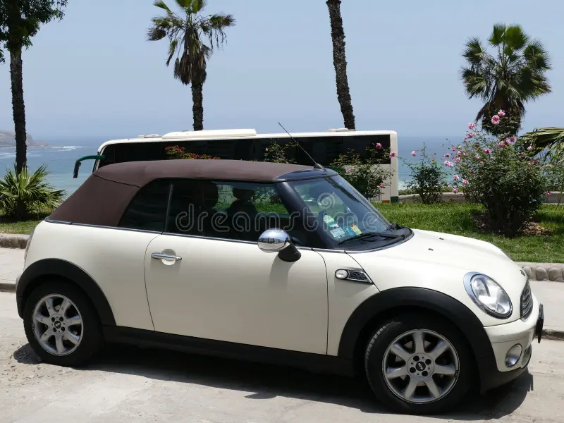 Lima, Peru. October 12, 2017. Side view of a mint condition white and brown color convertible Mini Cooper parked in Barranco district of Lima. In the image there are a park at coastline and the Pacific Ocean. The photo was taken on a sunny day. Bmw mini cooper car side view stock images, royalty-free photos and pictures