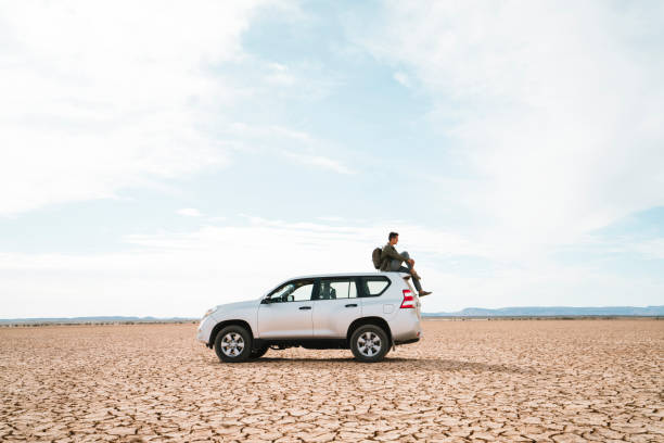 side view of man sitting on off-road vehicle at barren landscape against cloudy sky - car side view road foto e immagini stock