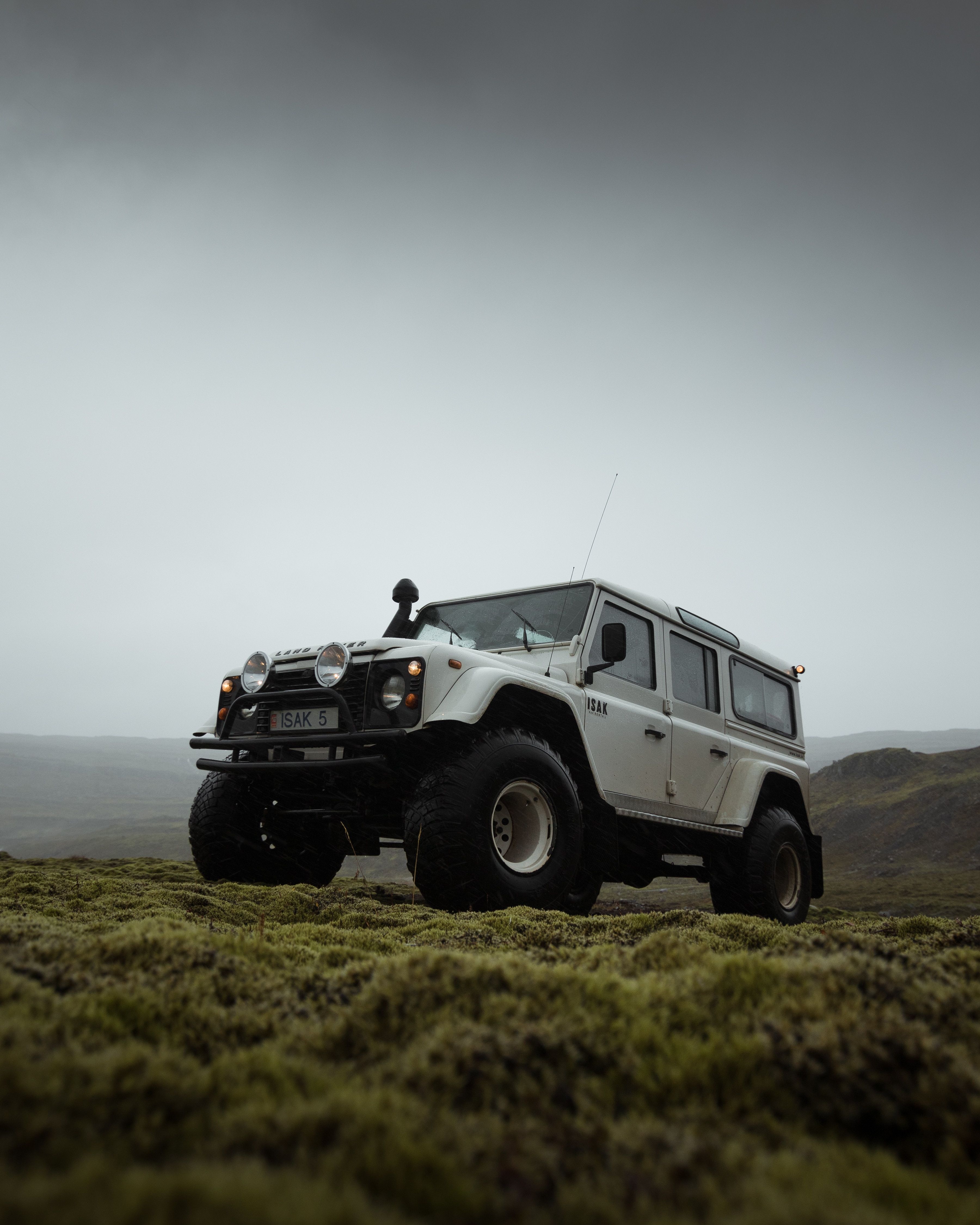 an off - road vehicle parked on the side of a grassy hill with dark clouds in the background