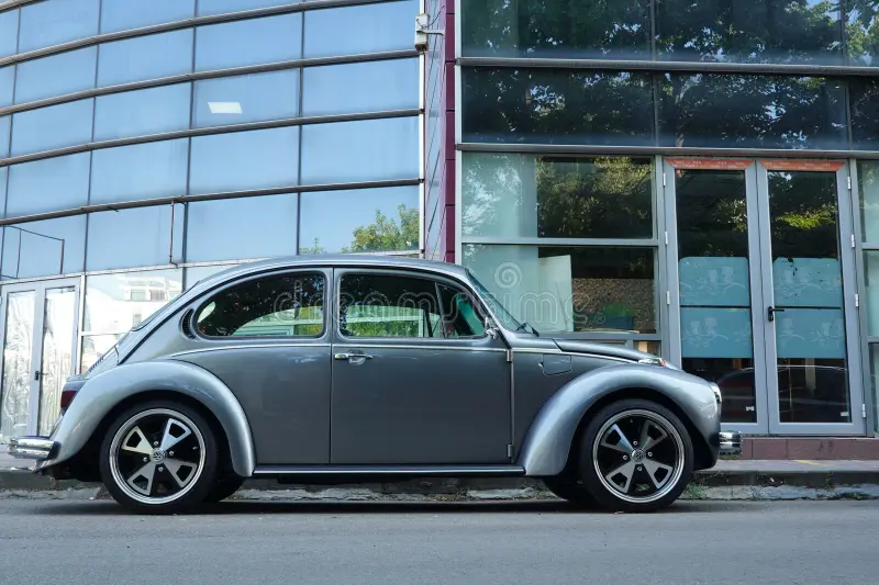 Closeup side view of retro Volkswagen Beetle silver car parked in front of office glass building. Vw beetle side view stock images, royalty-free photos and pictures